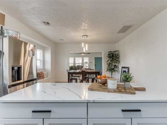 kitchen with visible vents, light stone countertops, stainless steel fridge, and a textured ceiling