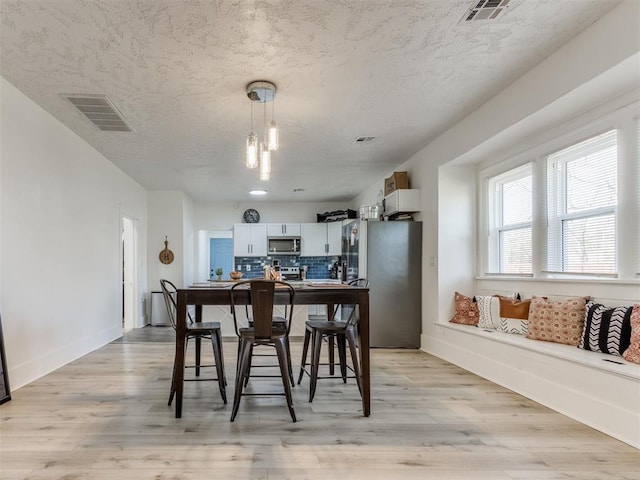 dining area with a textured ceiling, light wood-style floors, and visible vents