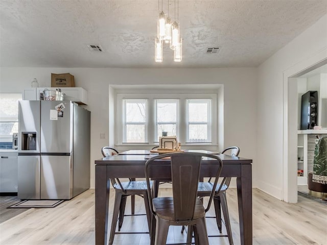 dining area with light wood-type flooring, a textured ceiling, a chandelier, and visible vents