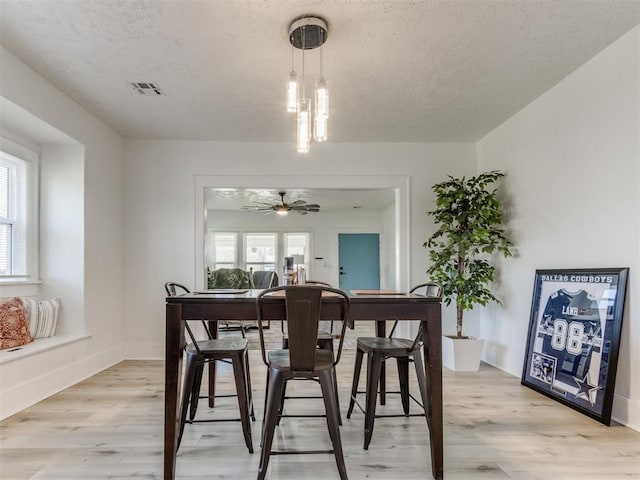 dining area featuring baseboards, a textured ceiling, light wood-style floors, visible vents, and ceiling fan