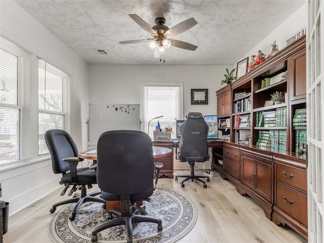 office space with ceiling fan, plenty of natural light, light wood finished floors, and a textured ceiling