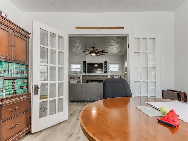 office area with a ceiling fan, light wood-style floors, a fireplace, and a textured ceiling
