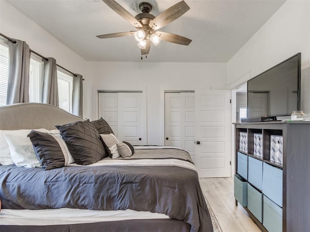 bedroom with ceiling fan, light wood-type flooring, and two closets