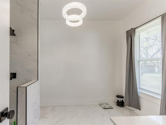 full bathroom featuring marble finish floor, baseboards, tiled shower, and an inviting chandelier