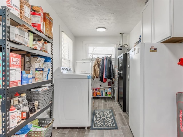 clothes washing area featuring water heater, wood finish floors, a textured ceiling, cabinet space, and washing machine and dryer