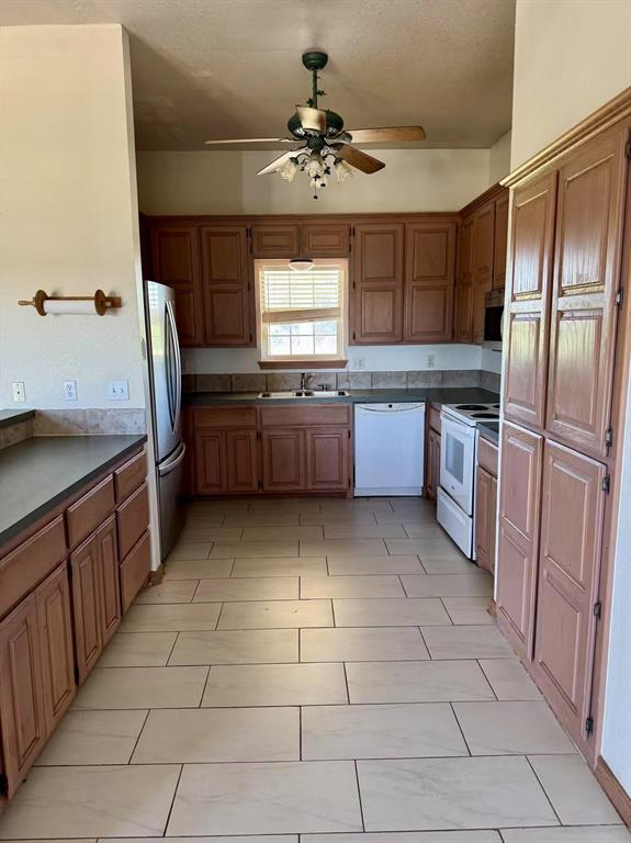 817 SW 16th St, Newcastle, OK 73065 - kitchen featuring appliances with stainless steel finishes, a sink, a ceiling fan, dark countertops, and brown cabinetry