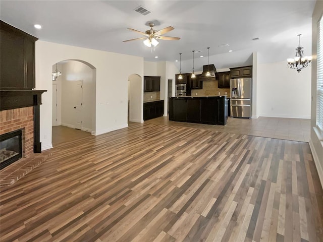 unfurnished living room with visible vents, a fireplace, wood finished floors, arched walkways, and ceiling fan with notable chandelier