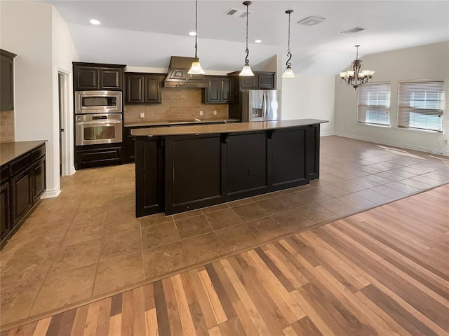 kitchen featuring decorative backsplash, custom exhaust hood, stainless steel appliances, a spacious island, and an inviting chandelier