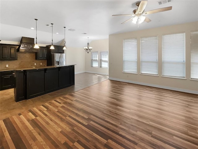 interior space with decorative backsplash, stainless steel refrigerator with ice dispenser, custom range hood, open floor plan, and ceiling fan with notable chandelier