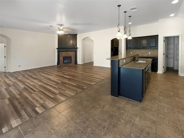 kitchen featuring a ceiling fan, arched walkways, a fireplace, and visible vents