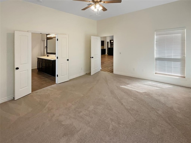 unfurnished bedroom featuring baseboards, carpet floors, connected bathroom, and a ceiling fan
