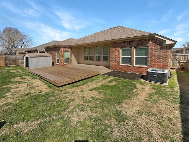 rear view of house featuring an outdoor structure, a fenced backyard, a storage unit, central AC, and a yard