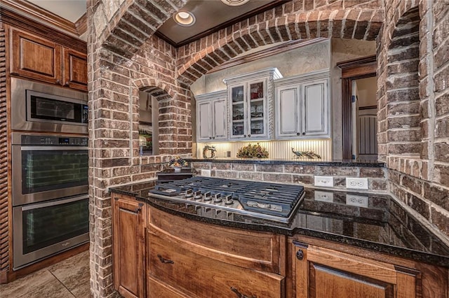 8301 NW 146th St, Oklahoma City, OK 73142 - kitchen with glass insert cabinets, dark stone counters, brick wall, and stainless steel appliances
