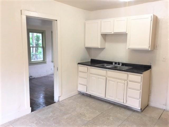 2921 NW 12th St, Oklahoma City, OK 73107 - kitchen with baseboards, white cabinetry, a sink, and dark countertops