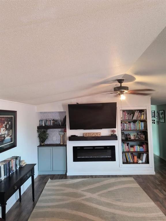 living area with a glass covered fireplace, wood finished floors, a textured ceiling, and ceiling fan