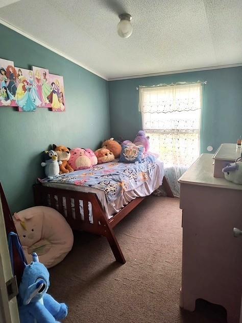 bedroom featuring a textured ceiling, vaulted ceiling, carpet flooring, and crown molding