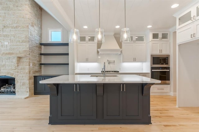 15632 Flora Ave, Edmond, OK 73013 - kitchen with wall oven, premium range hood, stainless steel microwave, white cabinetry, and light wood-style flooring