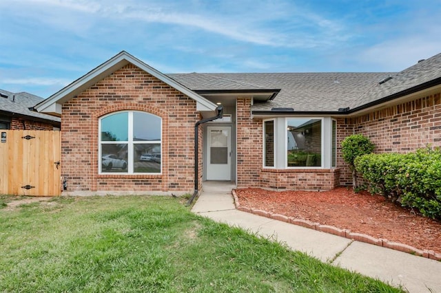 single story home with brick siding, a shingled roof, a front lawn, and a gate