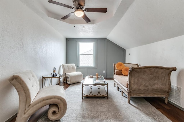 living area with vaulted ceiling, a textured wall, visible vents, and ceiling fan