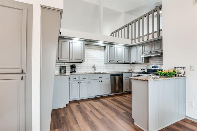 kitchen with stainless steel appliances, under cabinet range hood, a sink, and backsplash