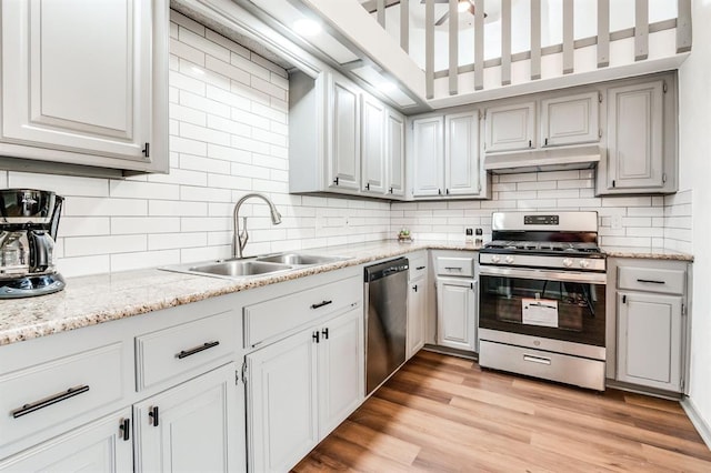 kitchen with under cabinet range hood, a sink, light wood-style floors, decorative backsplash, and appliances with stainless steel finishes