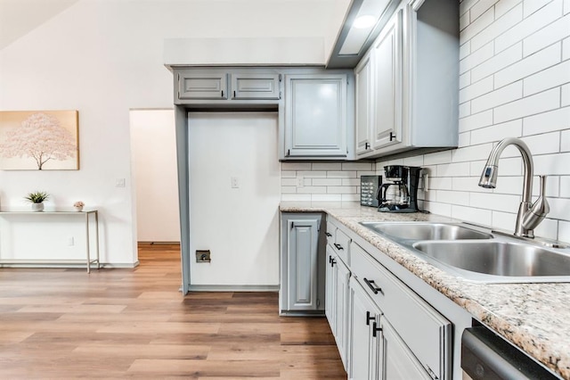 kitchen featuring light wood-type flooring, dishwasher, a sink, and backsplash