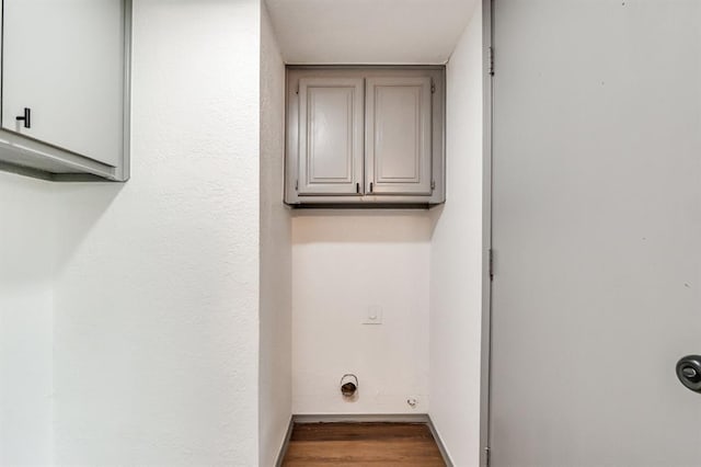 laundry room featuring electric dryer hookup, baseboards, wood finished floors, and cabinet space