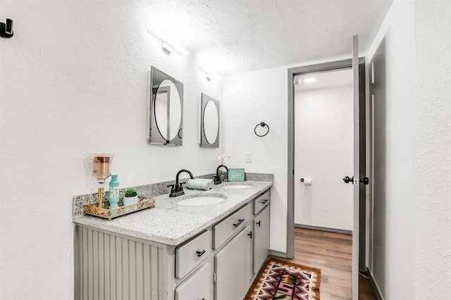 bathroom featuring wood finished floors, a sink, a textured ceiling, and double vanity