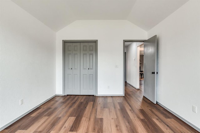 unfurnished bedroom featuring vaulted ceiling, a closet, baseboards, and wood finished floors