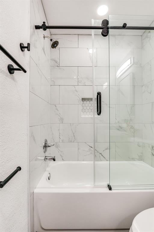 bathroom featuring toilet, a textured wall, and combined bath / shower with glass door