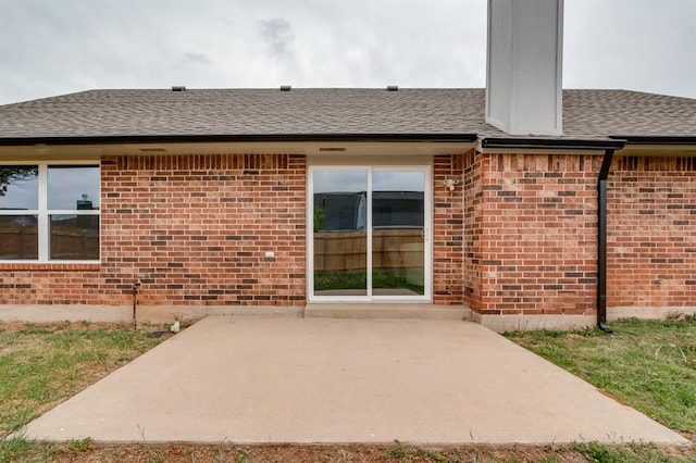back of property with a patio area, brick siding, and roof with shingles