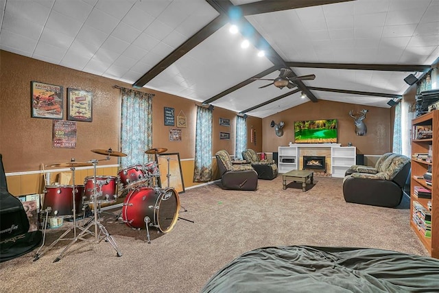 game room with a ceiling fan, vaulted ceiling with beams, a textured wall, a lit fireplace, and carpet flooring