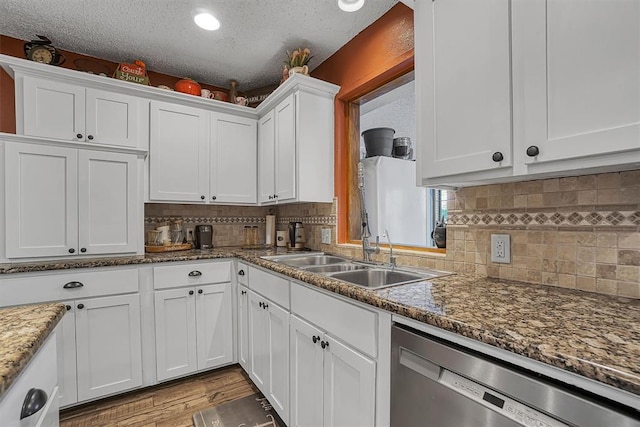 kitchen featuring white cabinets, stainless steel dishwasher, a sink, light wood-style floors, and tasteful backsplash