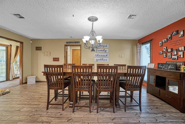 dining area with a notable chandelier, wood finished floors, a textured ceiling, and visible vents