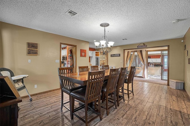 dining room featuring a chandelier, a textured ceiling, wood finished floors, and visible vents