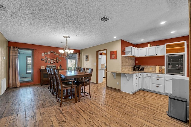 dining room with a textured ceiling, beverage cooler, light wood-style floors, an inviting chandelier, and visible vents