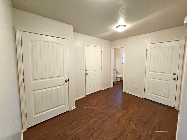 unfurnished bedroom featuring baseboards, dark wood-style flooring, and ensuite bath