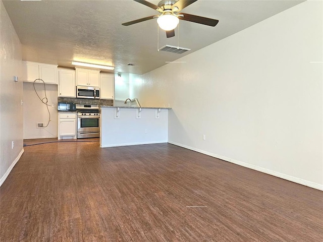 kitchen with white cabinets, visible vents, stainless steel appliances, dark wood-style floors, and backsplash