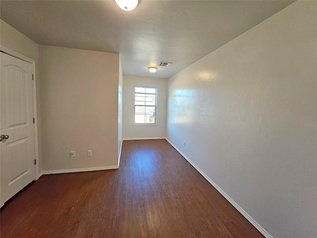 unfurnished room featuring dark wood-type flooring, baseboards, and visible vents