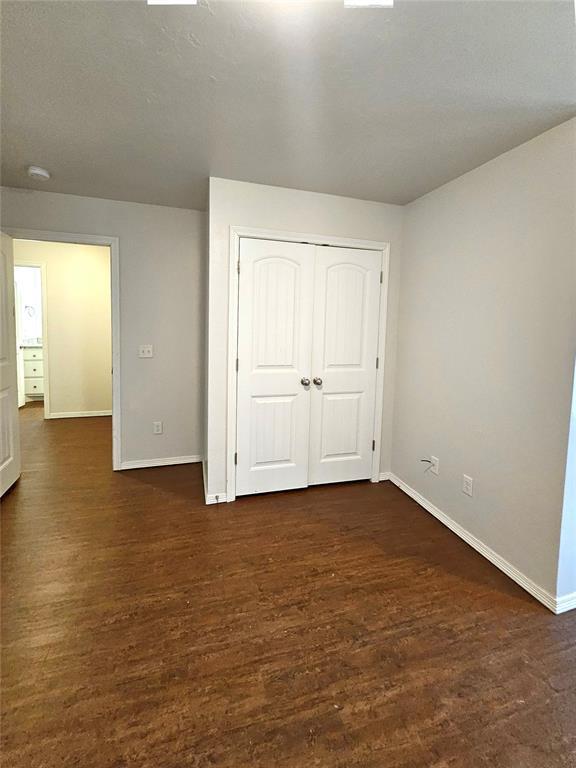 unfurnished bedroom with a closet, dark wood-style floors, and baseboards