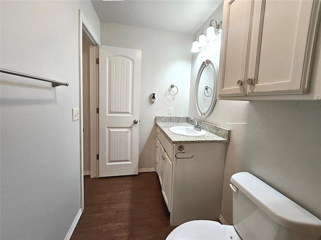 half bathroom featuring baseboards, toilet, vanity, and wood finished floors