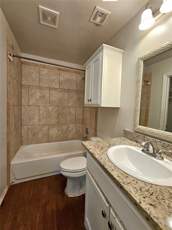bathroom featuring toilet, visible vents, wood finished floors, and shower / bath combination