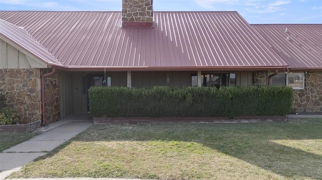 view of side of property featuring a chimney, a carport, stone siding, and a yard