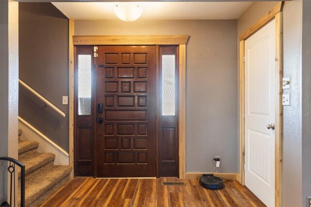 foyer entrance with visible vents, plenty of natural light, stairway, and wood finished floors