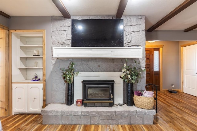 interior details featuring baseboards, beamed ceiling, a wood stove, and wood finished floors