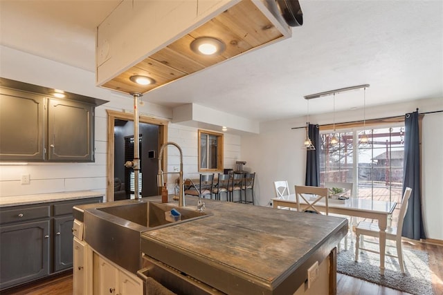 kitchen featuring a center island with sink, pendant lighting, a sink, and dark wood-type flooring