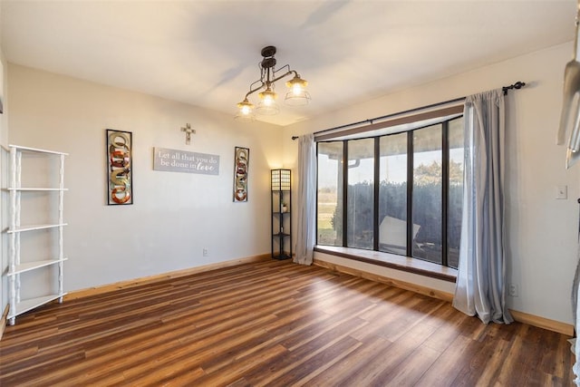 spare room with dark wood-style floors, baseboards, and an inviting chandelier