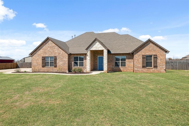 view of front of property featuring roof with shingles, brick siding, a front yard, and fence