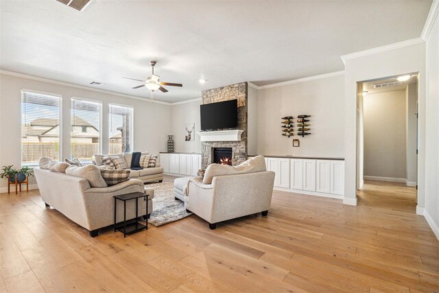 living room featuring baseboards, a fireplace, ornamental molding, ceiling fan, and light wood-type flooring