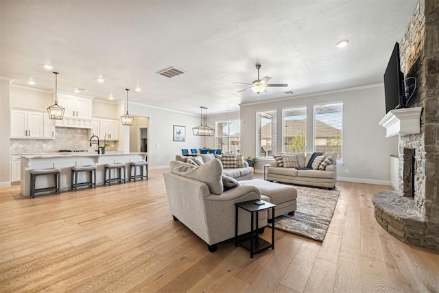 living room with crown molding, light wood-type flooring, visible vents, a ceiling fan, and a fireplace